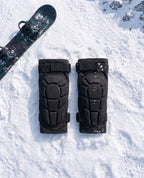 Pactline snow knee pads laid flat on snow beside a snowboard