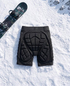 Pactline snow impact shorts laid flat on snow beside a snowboard