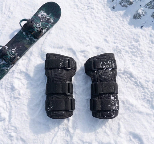 Pactline snow wrist guards laid flat on snow beside a snowboard