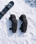 Pactline snow elbow pads laid flat on snow beside a snowboard